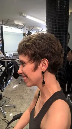 Corte curto cacheado com volume no alto, cliente sorrindo